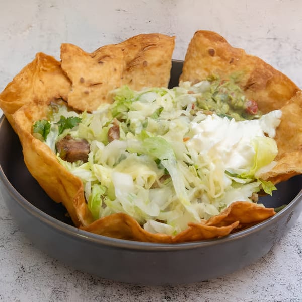 A taco salad in a crispy tortilla bowl, topped with lettuce, guacamole, and sour cream.