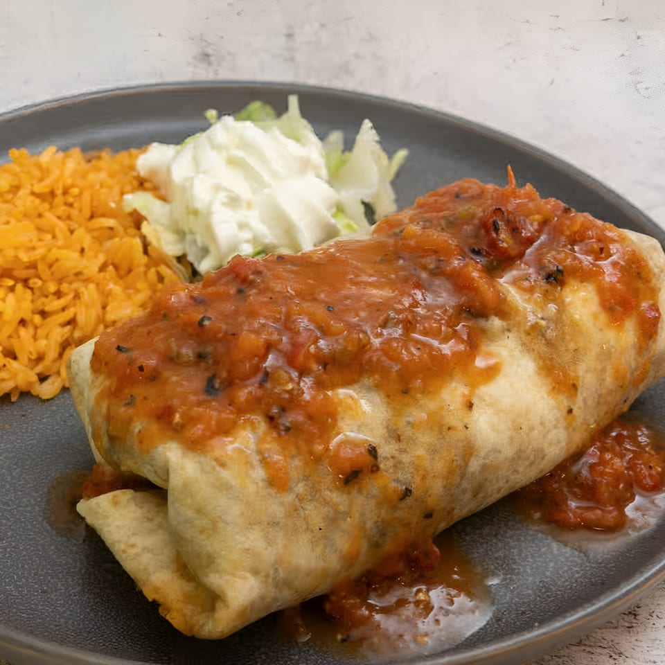 El Que Pasa's burrito covered in red salsa, with a side of rice and coleslaw.