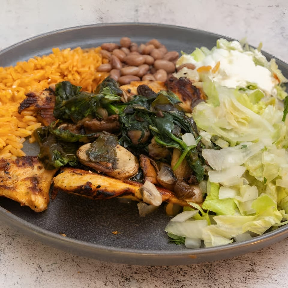 El Que Pasa's grilled chicken with rice, beans, sautéed spinach, mushrooms, and a side salad.
